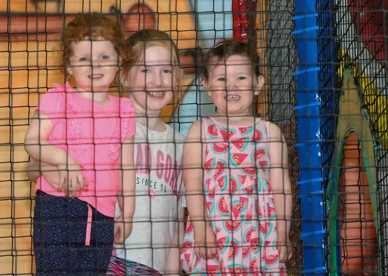 Three girls smiling together inside the play frame