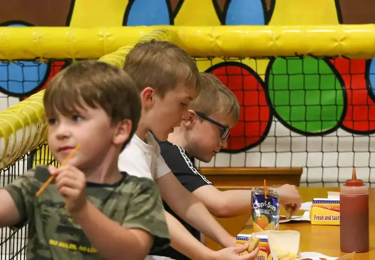 Three boys eating chips and sausages at a party table