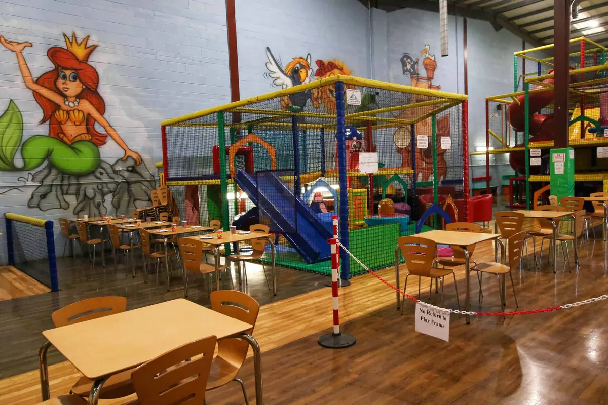 Café tables and chairs right beside the play frames, under a mermaid mural